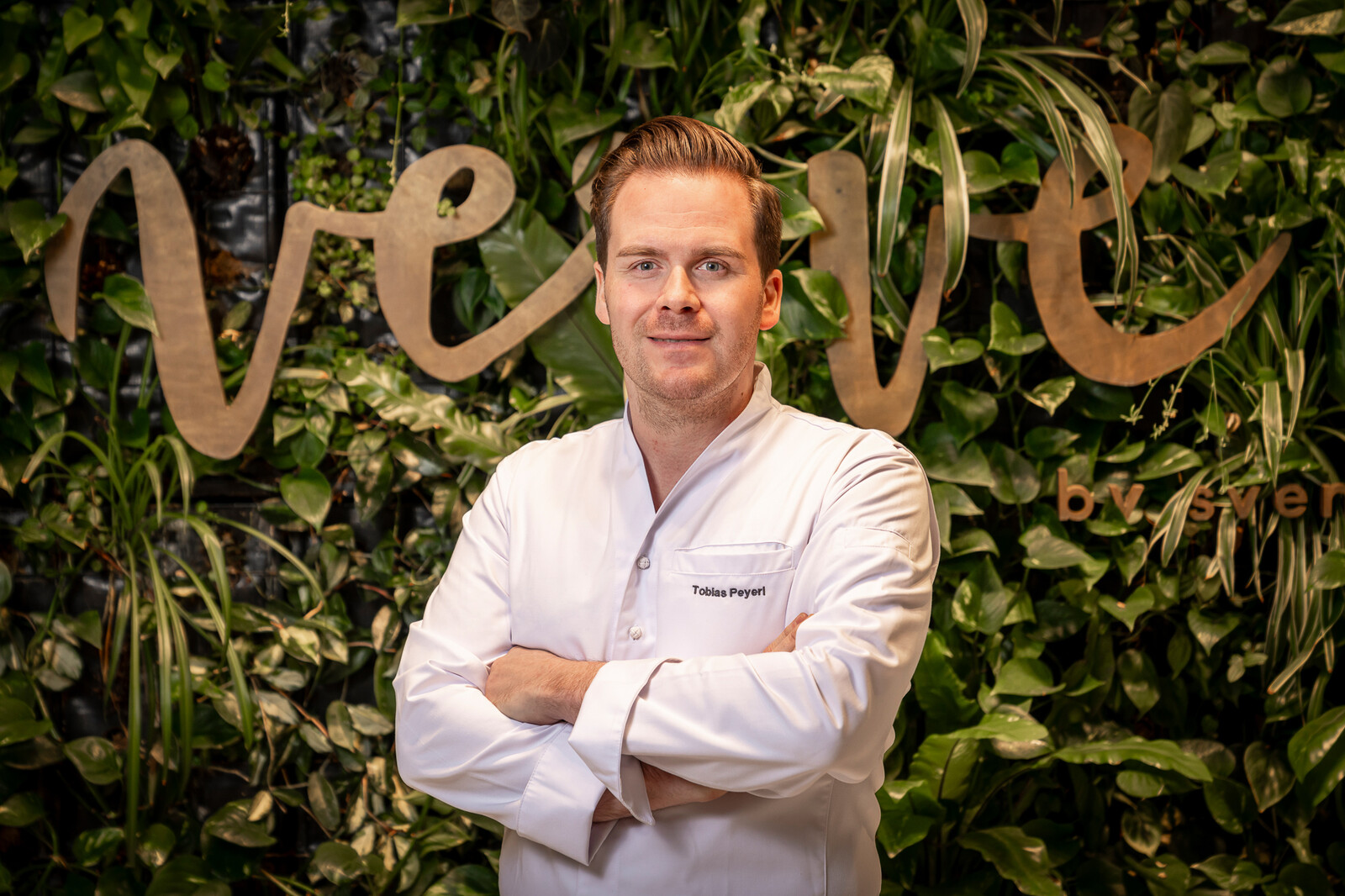 Der neue Executive Sous Chef, des Restaurant Verve by sven, Tobias Peyerl steht vor einer Grünen mit Pflanzen bedeckten Wand hinter ihm steht der Schriftzug "Verve". Das Restaurant Verve by sven befindet sich im Grand Resort Bad Ragaz, einem Luxushotel in der Schweiz. Das Verve by Sven hat einem Michelin Stern, 15 Gault-Millau-Punkte und 92 Falstaff-Punkte.