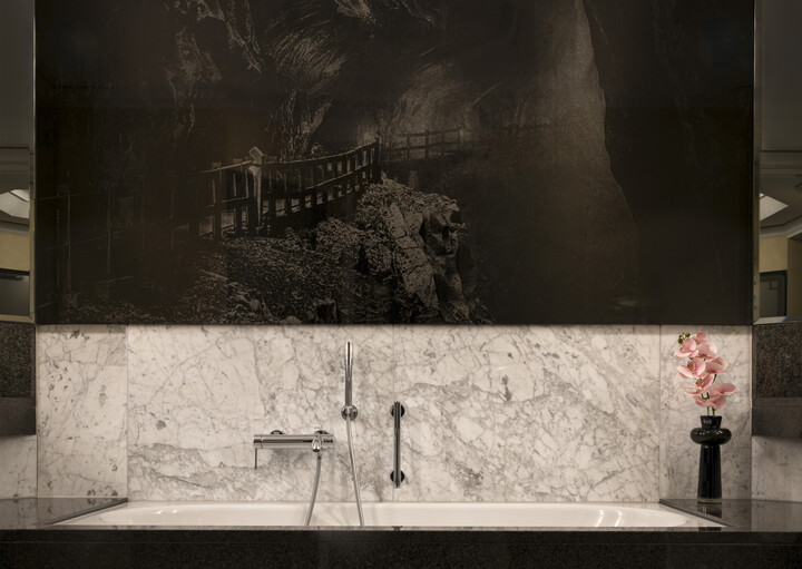 Luxuriöses Badezimmer mit weisser Marmorbadewanne, Akzenten aus poliertem schwarzem Stein und einer auffälligen schwarz-weissen Wandmalerei in den Bergen. Elegante und heitere Atmosphäre.