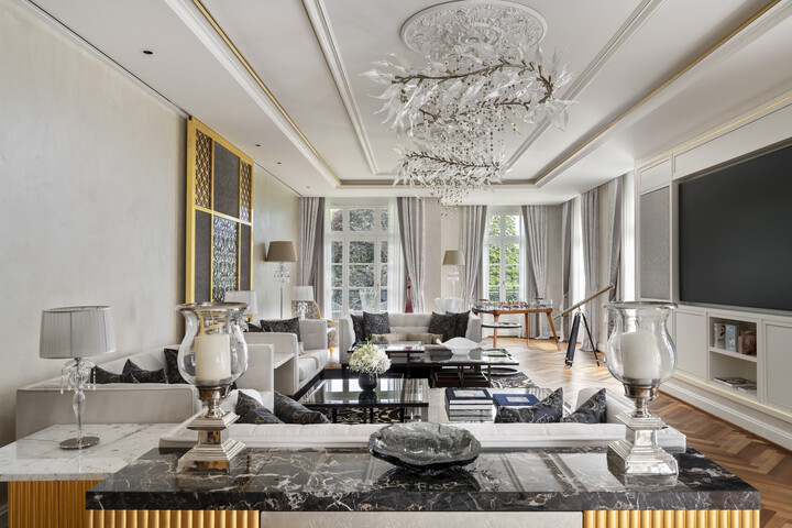 Elegantes Wohnzimmer der King Suite in Weiss- und Grautönen mit luxuriösem Kronleuchter, Marmorakzenten, grossen Fenstern, modernen Möbeln und einem grossen Fernseher.