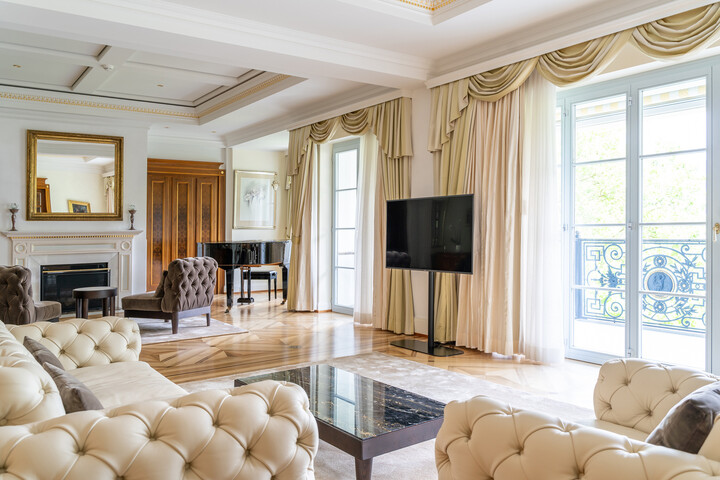 Elegantes Wohnzimmer der Royal Suite mit gepolsterten Sofas, einem Marmor-Couchtisch und einem Kamin mit großem Spiegel. Ein Flügel und raumhohe Vorhänge sorgen für zusätzliche Luxusausstrahlung.