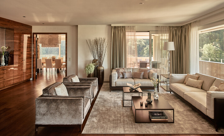 Luxuriöses Wohnzimmer der Penthouse Suite mit weichen Sofas, dekorativen Kissen und einem zentralen Couchtisch. Warme Beleuchtung und große Fenster schaffen eine gemütliche, elegante Atmosphäre.