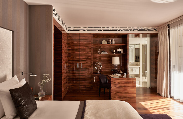 Elegantes Zimmer der Presidential Suite mit edlen Holzvertäfelungen und moderner Einrichtung. Ein Bett mit weißer Bettwäsche, ein Schreibtisch mit einem Globus und eine gut beleuchtete, luftige Atmosphäre.