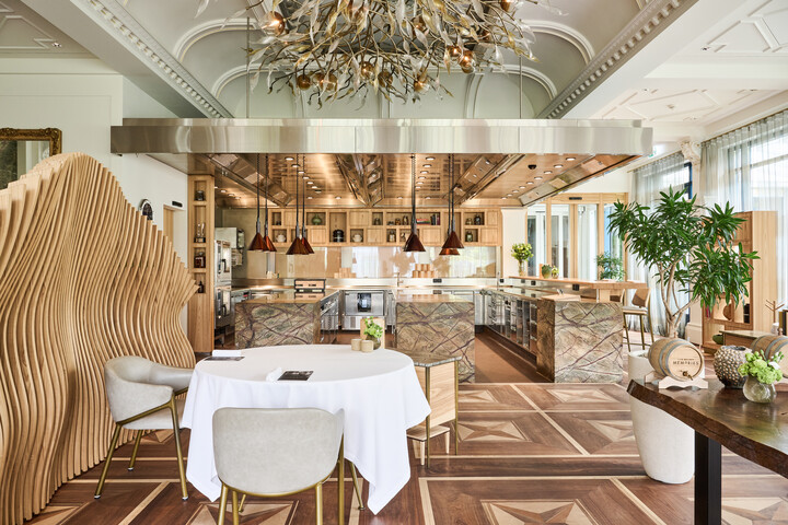 Stilvolle, moderne Küche und Essbereich mit Holz- und Marmorakzenten des Restaurant Sven Wassmer Memories. Mit einer skulpturalen Holztrennwand, eleganten Kronleuchtern und üppigem Grün.