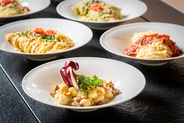 Eine Vielzahl von Pastagerichten wird elegant in weißen Schüsseln auf einem dunklen Tisch präsentiert. Jedes Gericht besticht durch unterschiedliche Zutaten und Saucen und sorgt so für eine lebendige und appetitliche Präsentation.