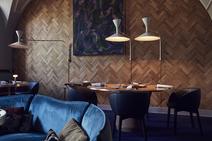 Das Restaurant Igniv wird von innen gezeigt. Ein Tisch, der von zwei Lampen beleutet wird, steht in der Mitte. Die Ecke eines blauen Sofas ist auf der linken Seite zu erkennen. Das Restaurant gehört zum Grand Resort Bad Ragaz. Das ist ein Sterneresort in der Schweiz.