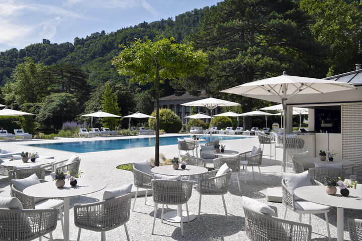 Der Himmel spiegelt sich auf der klaren Oberfläche des Thermal Wassers in dem Garten Pool des Hotel Grand Resort Bad Ragaz. Bäume und Berge befinden sich im Hintergrund des Pools. Das Hotel ist ein Superior Sterneresort in der Schweiz.