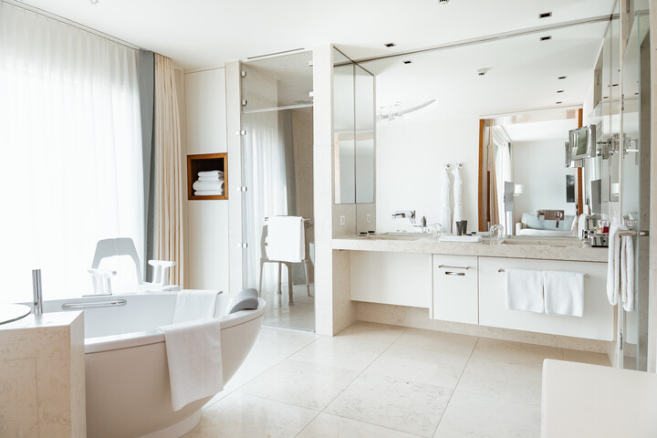 Modernes Badezimmer mit freistehender Badewanne, großem Spiegel und viel Tageslicht dank raumhoher Vorhänge. Minimalistisches und ruhiges Ambiente.