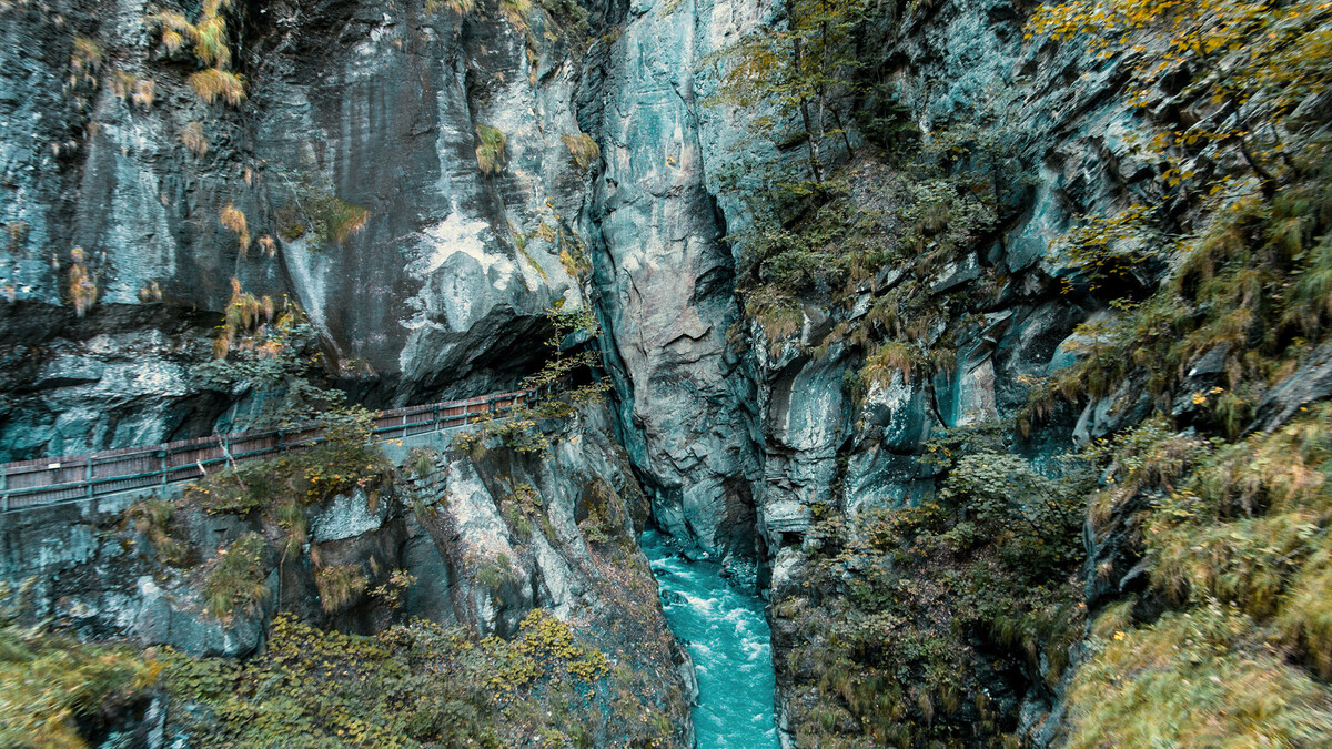 The path can be seen between the rocks of the Tamina Gorge. The water flows through the middle of the lower edge of the picture. Bushes and grass grow up the rocks to the left and right of the edges.