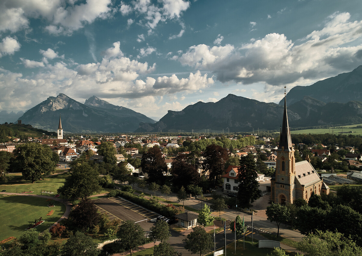 Das Dorf Bad Ragaz ist leicht von oben zu sehen. Wolken sind am Himmel und Berge befinden sich im Hintergrund. Ganz vorne ist das Grand Resort Bad Ragaz ersichtlich, ein Superior Sternehotel in der Schweiz.