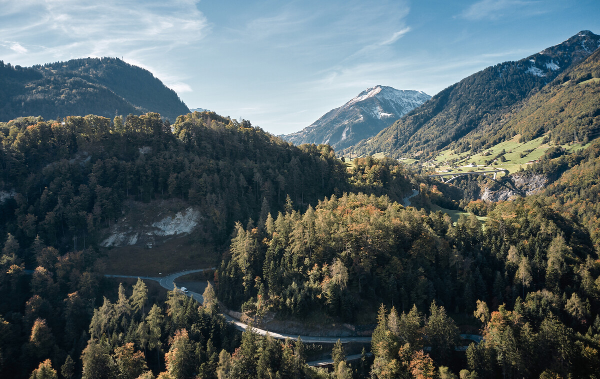Die Taminabrücke verbindet zwei Hügel miteinander. Nebst der Strasse ist durch die Bäume nicht viel auf dem Berg zu erkennen. Im Hintergrund befinden sich Bergspitzen. In der Nähe dieser Brücke befindet sich das Superior Hotel Grand Resort Bad Ragaz, ein Sternehotel in der Schweiz.