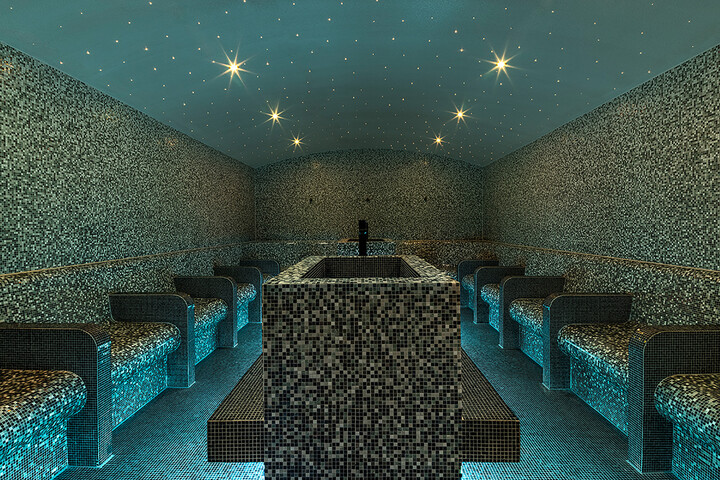 Luxuriöses, gefliestes Dampfbad mit Sitzgelegenheiten entlang der Wände. Die Decke ist mit sanften, sternförmigen Lichtern verziert, die eine ruhige und entspannende Atmosphäre schaffen.