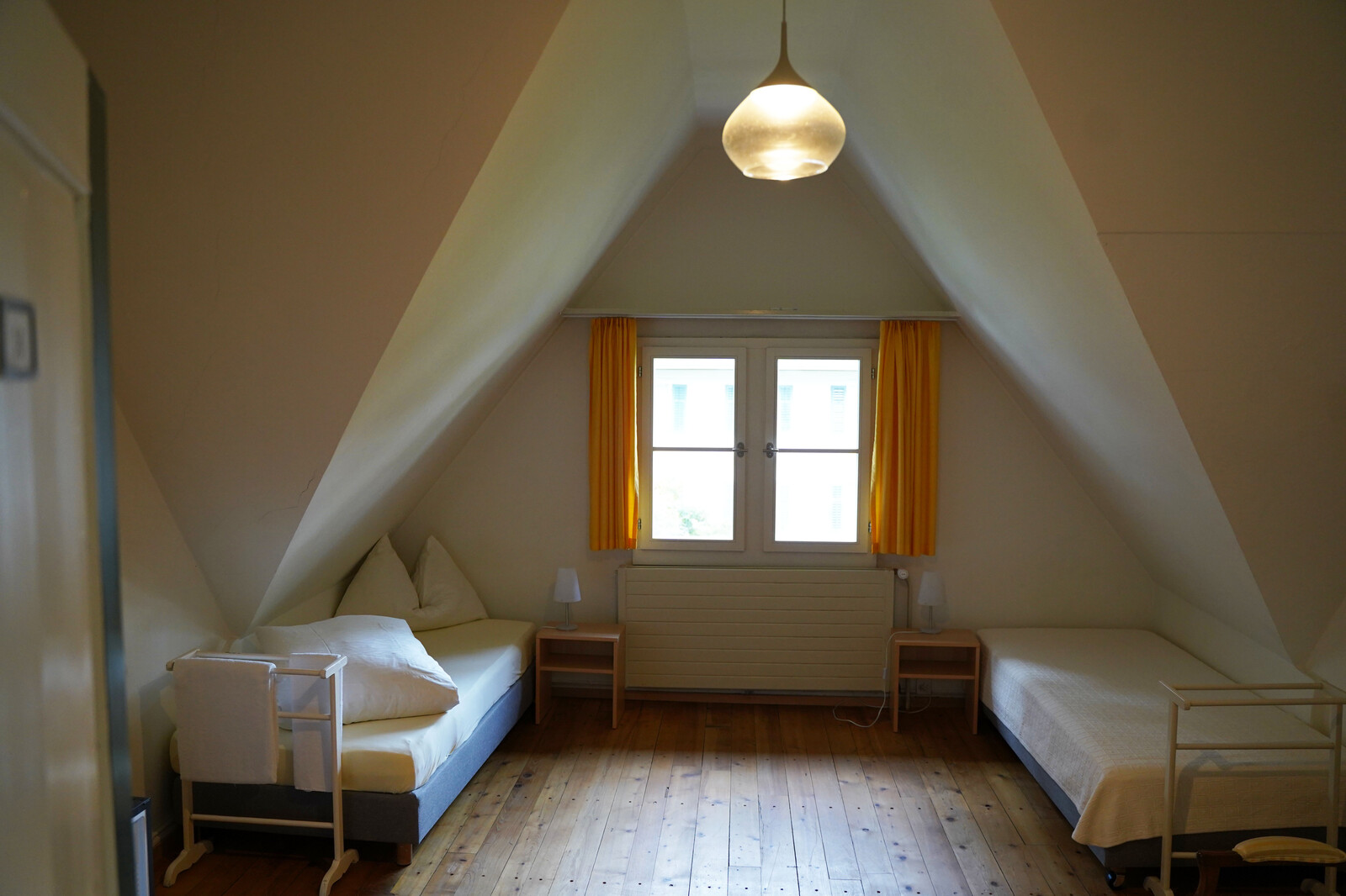 One of the rooms in the Hermitage staff house can be seen. There are two beds with bedside tables in this room. The staff house is located in Bad Ragaz and is part of the Hotel Grand Resort Bad Ragaz.