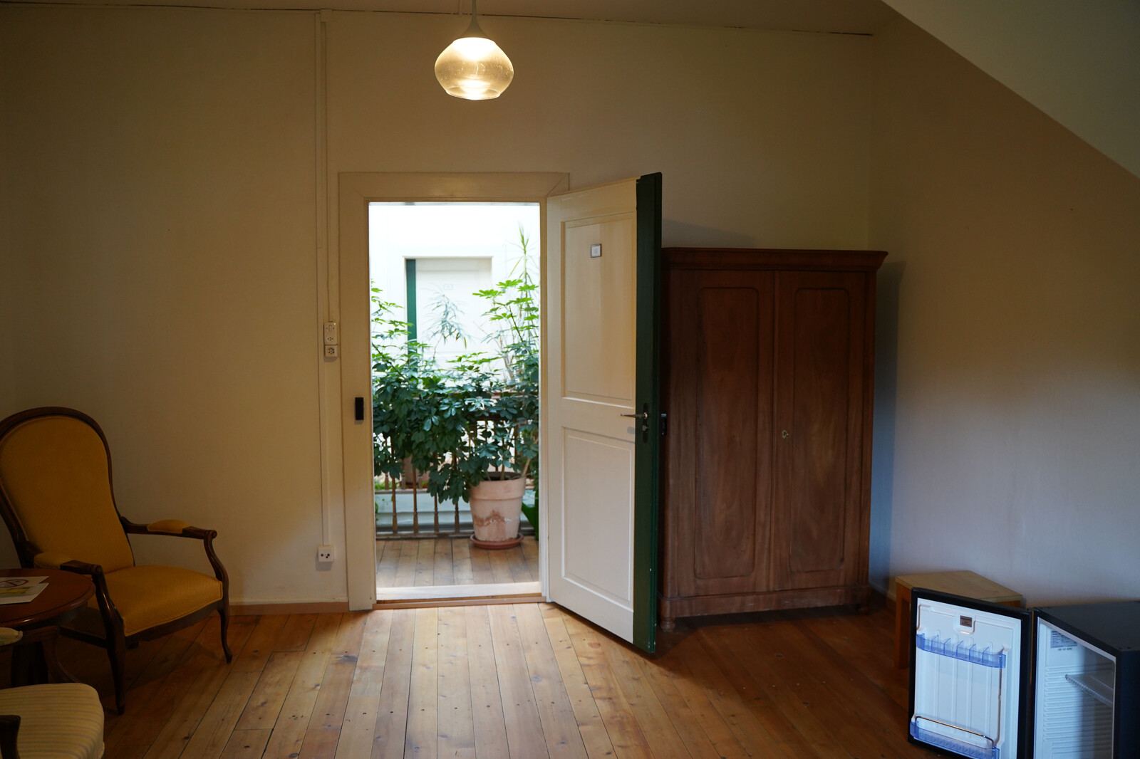Here you can see a room in the Hermitage staff house on Hermitageweg in Bad Ragaz. A cupboard and a chair can be seen next to the open door. Behind the door is the corridor, decorated with plants. The staff house belongs to the Hotel Grand Resort Bad Ragaz.