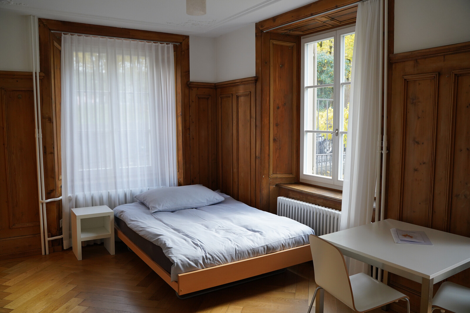 The studio in the Sarona staff house at the Grand Resort Bad Ragaz shows a bed and a table with chairs. The Grand Resort is a star hotel in Switzerland.