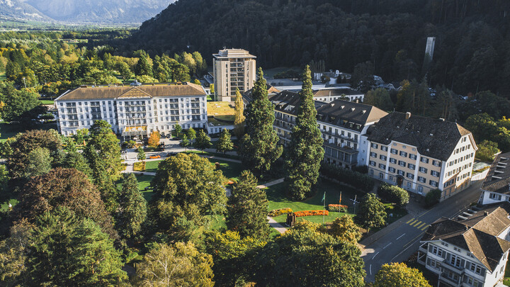 Alle drei Hotels, inklusive dem Spa Tower und dem Park des Grand Resort Bad Ragaz sind von vorne oben zu sehen. Auf der rechten Seite befindet sich ein Berg. Das Grand Resort Bad Ragaz ist ein Superior Sternehotel in der Schweiz.